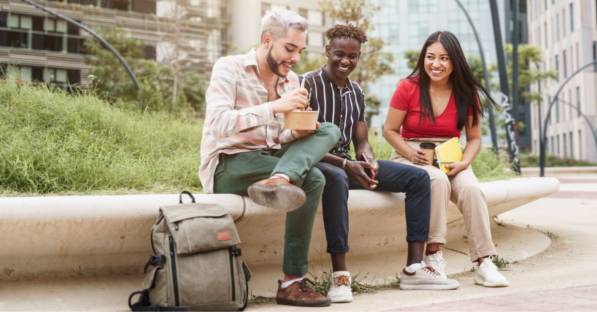 Group of three young adults sitting outside and enjoying a meal together